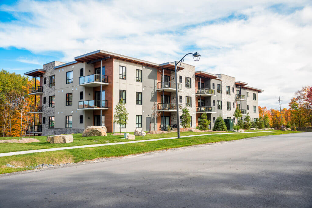 Modern four-story building with balconies, surrounded by lush green landscaping.