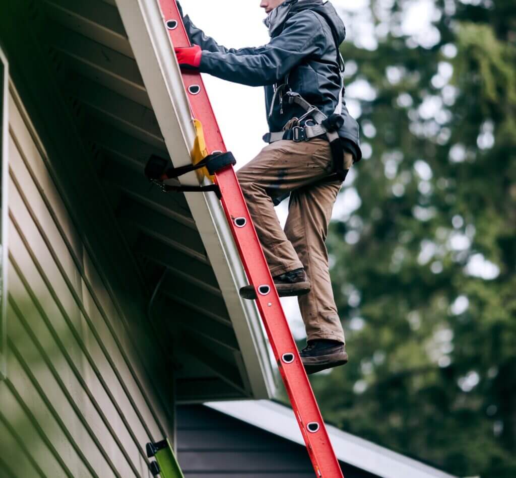 Worker on red ladder performing exterior home maintenance near roof.