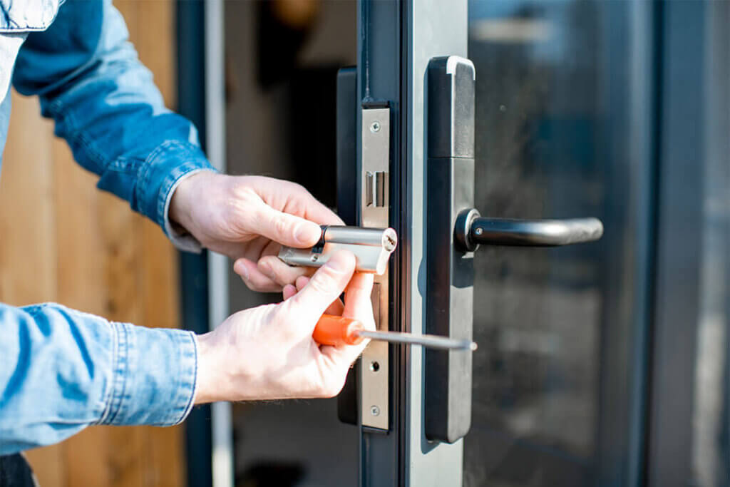 Installing a metallic lock on a glass door; a hand holds a screwdriver.