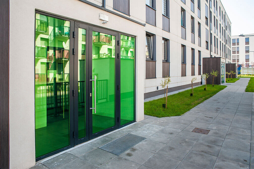 Green commercial exterior doors on a modern building, highlighting replacement services.