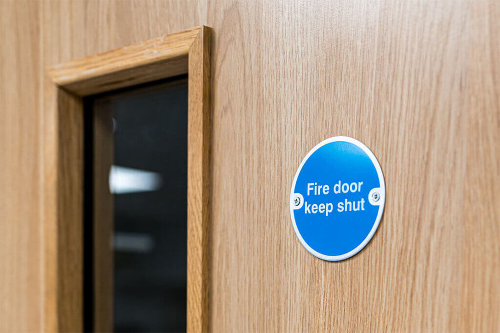 Wooden door with a blue sign reading "Fire door keep shut."