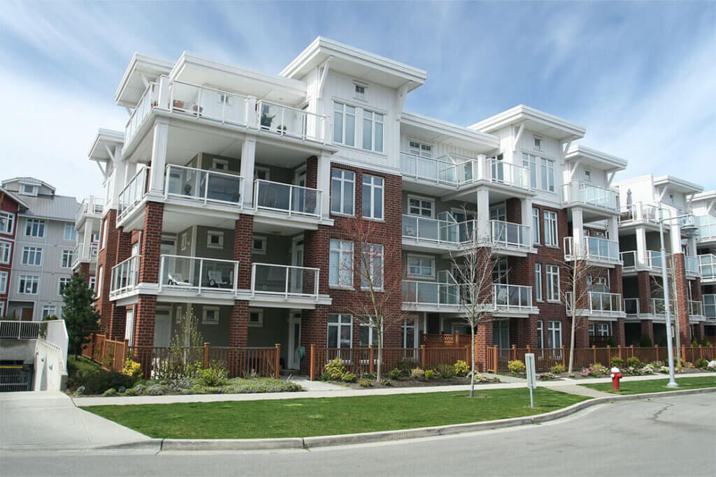 Four-story brick apartment building with white trim, surrounded by green lawns and paths.