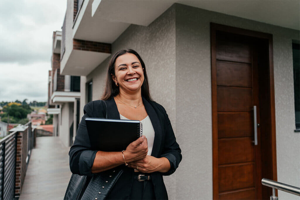 Person smiling holding a black folder outside a modern building with wooden doors.
