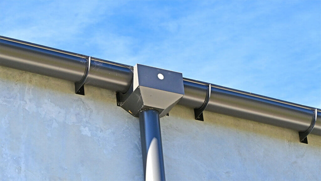 Black commercial rain gutters on a building against a clear blue sky.