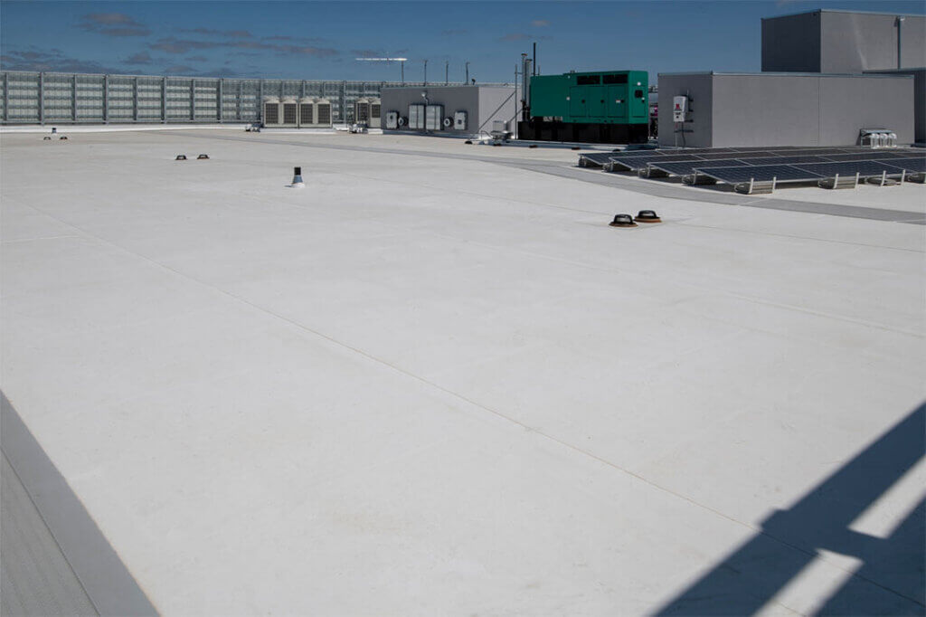 Flat commercial roof, light gray, with solar panels and green equipment in the background.