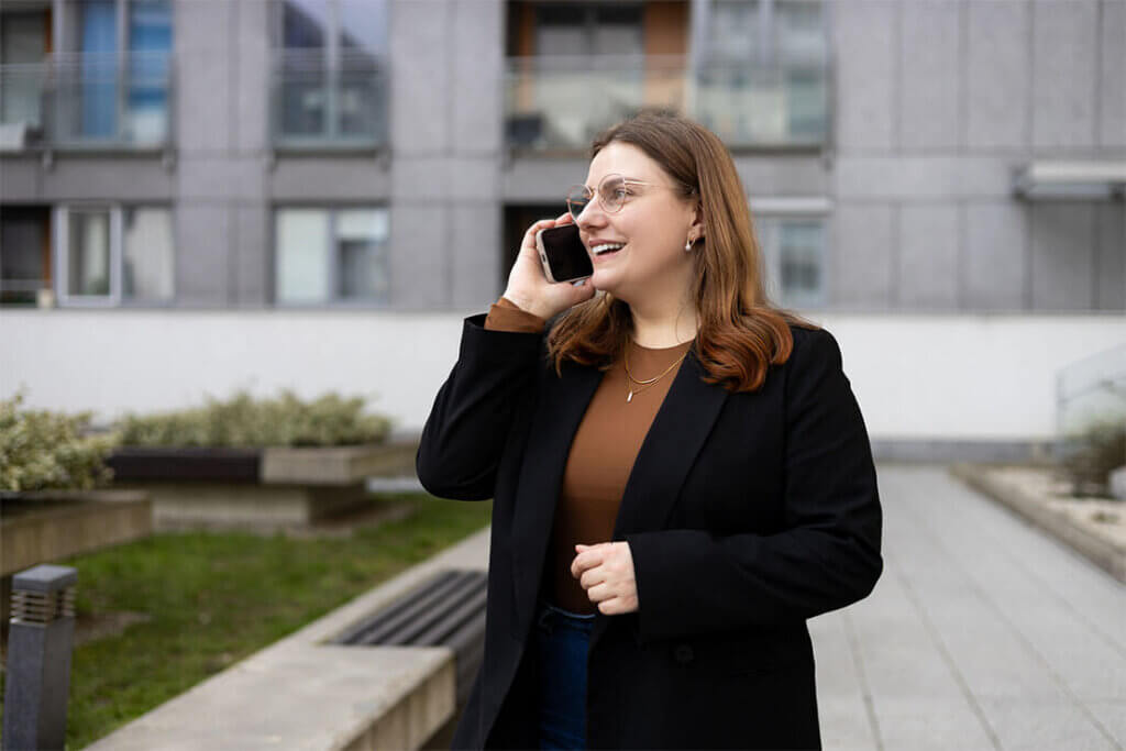 Person in a black coat using a smartphone outside a gray commercial building.