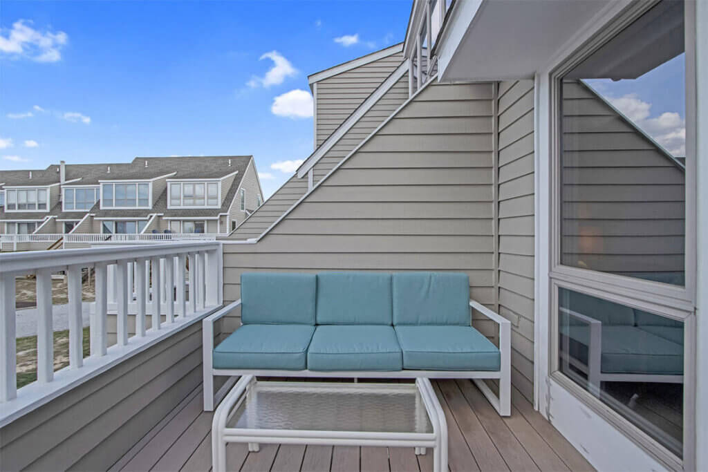 Residential balcony with light blue seating and gray siding under a clear sky.