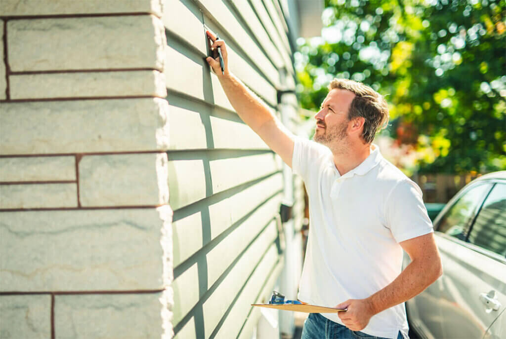 Person inspecting light gray commercial siding installation, holding a clipboard.