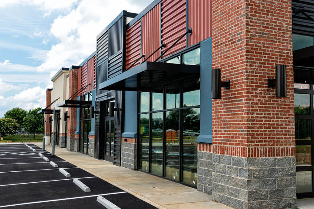 Commercial building with brick and panel siding, large windows, and black awnings.