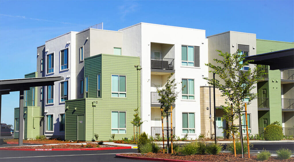 Modern building with light green siding, white facade, and balconies. Text reads: "No Parking Fire Lane".
