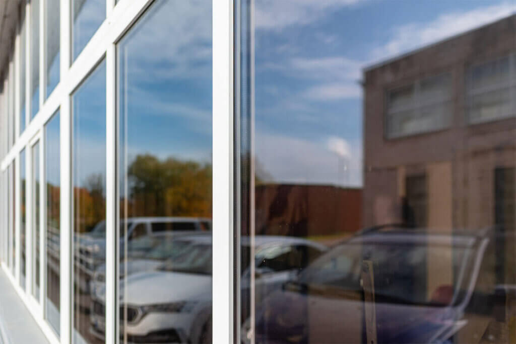 Reflective glass windows on a commercial building, showing cars and sky.