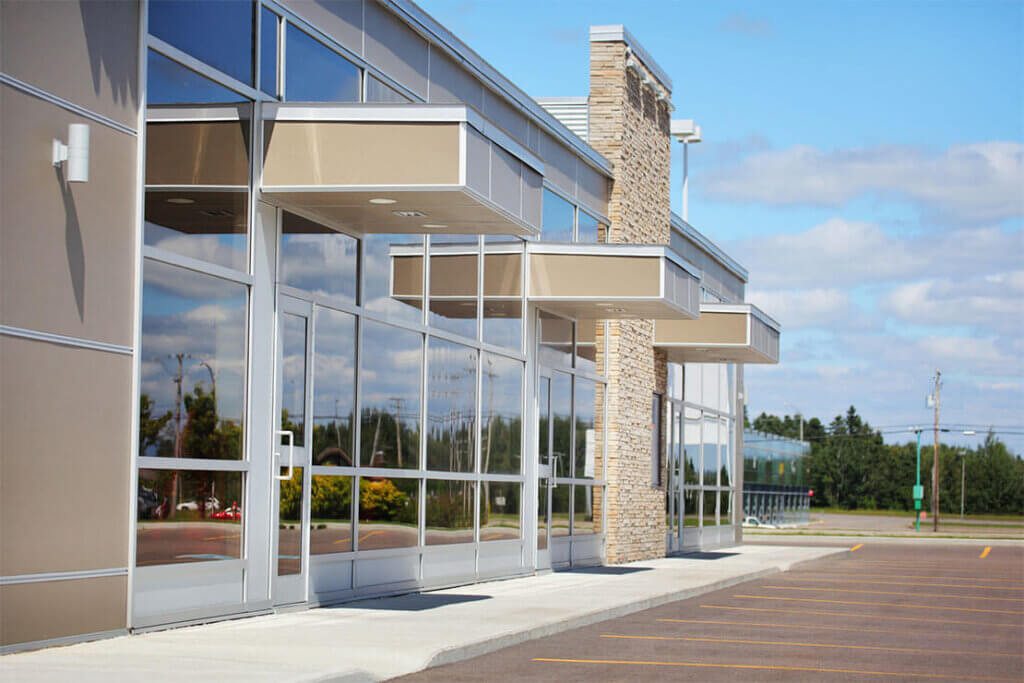 Modern commercial building with large glass windows and beige awnings.